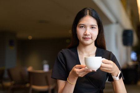Young Asian woman sitting in coffee shop wearing stylish black dressの写真素材