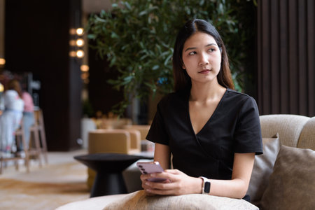 Young Asian woman sitting in coffee shop wearing stylish black dressの写真素材