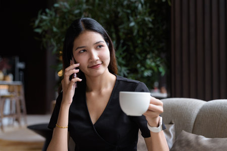 Young Asian businesswoman sitting in coffee shop wearing stylish black dress drinking coffeeの写真素材