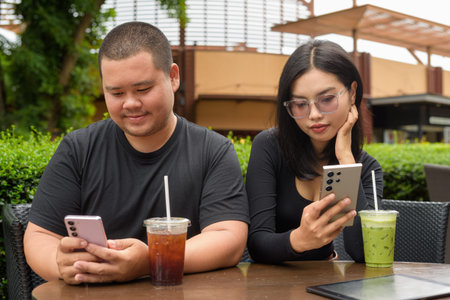 Happy Asian couple sitting together in outdoors cafe restaurant during summer
