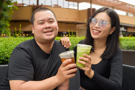 Happy Asian couple sitting together in outdoors cafe restaurant during summer