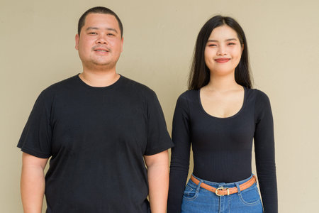 Portrait of young Asian couple against plain wall background