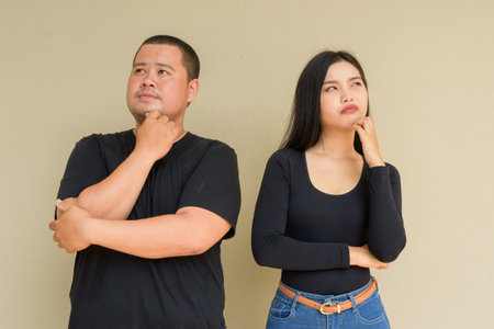 Portrait of young Asian couple against plain wall background thinkingの写真素材