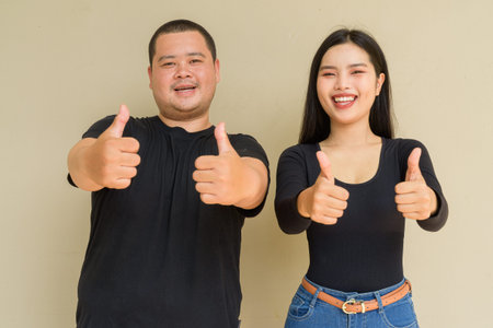 Portrait of young Asian couple against plain wall background