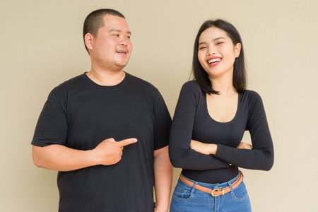 Portrait of young Asian couple against plain wall background