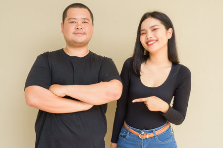Portrait of young Asian couple against plain wall background