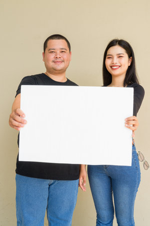 Portrait of young Asian couple against plain wall backgroundの写真素材