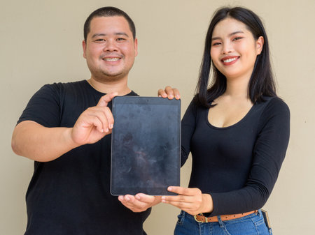 Portrait of young Asian couple against plain wall backgroundの写真素材