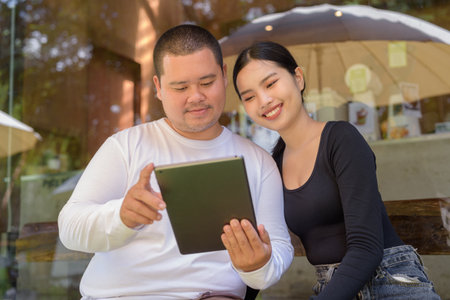 Asian ouple sitting and using digital tablet computer in coffee shopの写真素材