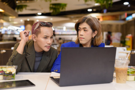 Gender diverse Asian coworkers eating salad and working digitally