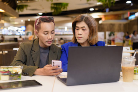 Gender diverse Asian coworkers eating salad and working digitally