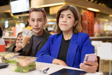Gender diverse Asian coworkers eating salad and working digitallyの写真素材