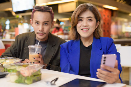 Gender diverse Asian coworkers eating salad and working digitally