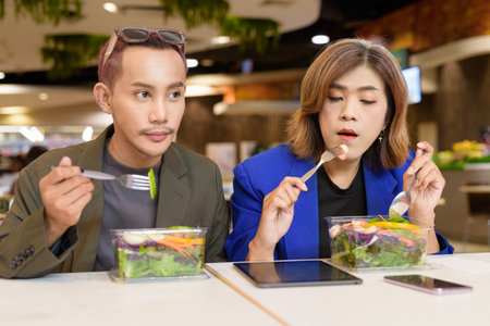 Gender diverse Asian coworkers eating salad and working digitallyの写真素材