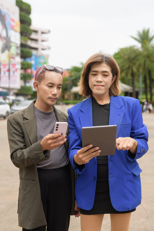 Asian gender diverse business coworker professionals using technology on city street