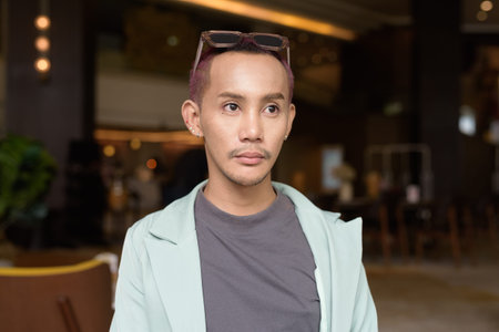 Non binary Asian gay man with makeup sitting in cafe