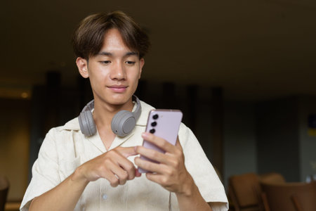 Non binary cute Asian student man sitting in modern coffee shop