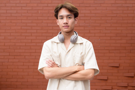 Portrait of non binary cute Asian young gay man against brick wall