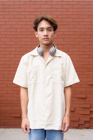 Portrait of non binary cute Asian young gay man against brick wall