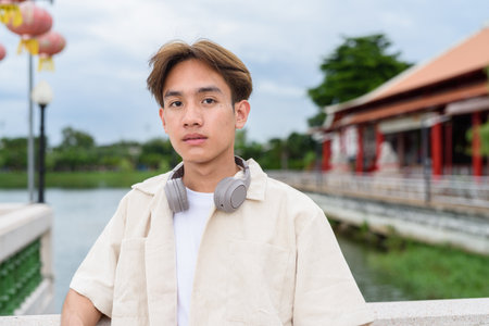 Asian non binary young tourist person with headphones relaxing at park near lakeの写真素材