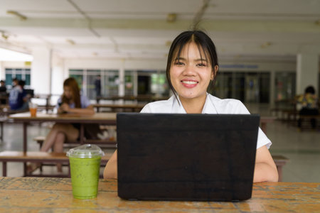 Thai teenage girl in university uniform sitting solo at a university campus coffee shop area....