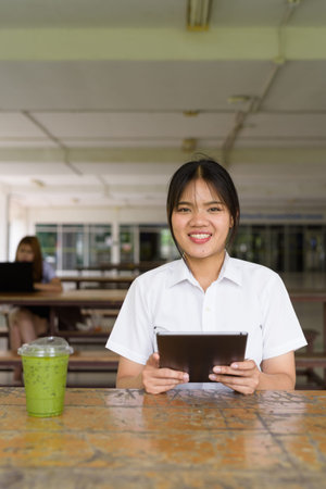 Thai teenage girl in university uniform sitting solo at a university campus coffee shop area....