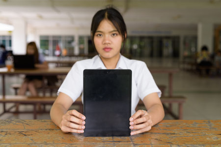 Thai teenage girl in university uniform sitting solo at a university campus coffee shop area....