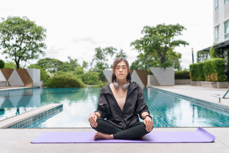Transgender woman performing yoga poses outdoors by pool, showcasing wellness, balance and morning health habitsの写真素材