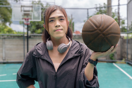 Portrait of a fit transgender woman standing on outdoor basketball court, promoting strength and urban fitness lifestyleの写真素材