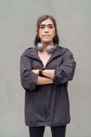 Portrait of a transgender Asian woman in front of a plain outdoors wall wearing sports clothing