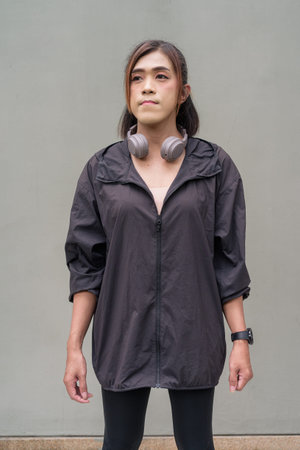 Portrait of a transgender Asian woman in front of a plain outdoors wall wearing sports clothing