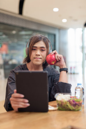 Mature transgender woman eating healthy salad with apple and water in casual mall restaurant environmentの写真素材