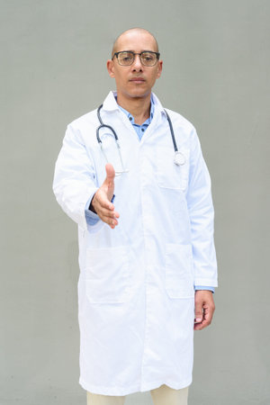 Portrait of mature bald male doctor wearing lab coat and eyeglasses with stethoscope around neck,...