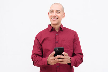 Confident bald adult man in burgundy button-down shirt standing against plain white background....