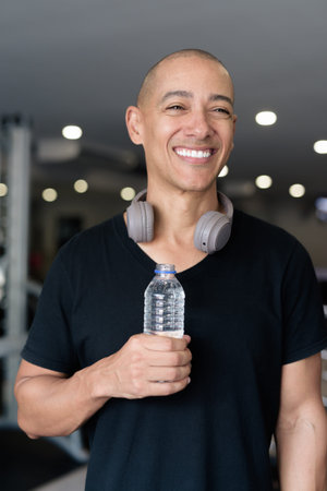 Bald Hispanic man training in gym for fitness and workout. Muscular male exercising indoors with...