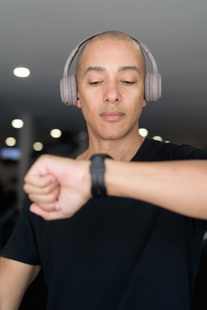 Hispanic bald man athlete in gym using smartwatch fitness tracker monitoring his exercise stats and heart rate with wearable technology in modern gymの写真素材
