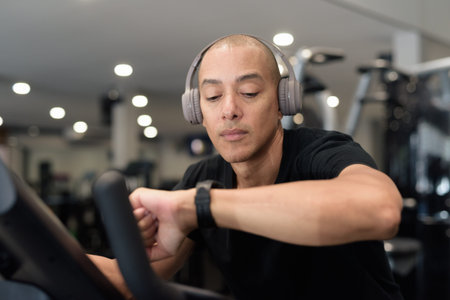 Hispanic bald man athlete in gym using smartwatch fitness tracker monitoring his exercise stats and...