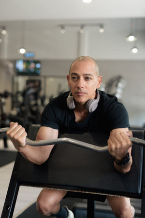 Bald Hispanic man training in gym for fitness and workout. Muscular male exercising indoors with...