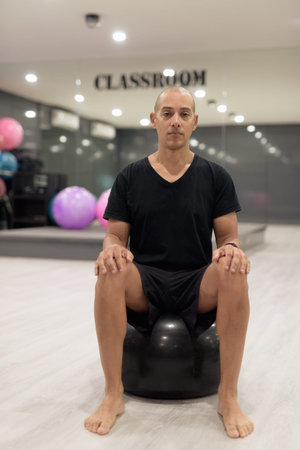 Bald Hispanic man training in gym for fitness and Pilates workout. Muscular male exercising indoors with confidence, wearing black shirt. Healthy lifestyle, strength and wellness focus.の写真素材