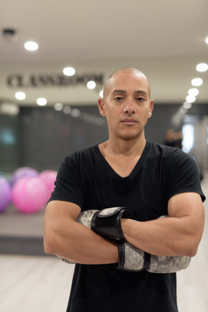Hispanic bald man wearing boxing gloves posing as fighter or coach inside modern gym classroom....