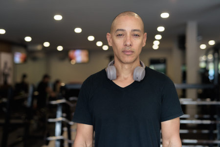 Bald Hispanic man training in gym for fitness and workout. Muscular male exercising indoors with...