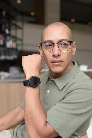 Latin man in his 40s posing in hotel cafe or bar with modern interior. Headshot ocused on elegant business-casual appearance, relaxed attitude, confidence, and handsome mature masculinity.の写真素材