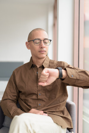 Hispanic man in his 40s sitting in coffee shop, wearing casual shirt and eyeglasses. Confident and happy expression. Urban lifestyle, modern man, adult portrait in relaxed environment.の写真素材