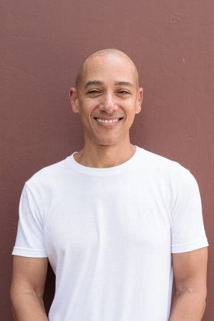 Bald Latin man against wall in casual white t-shirt. Minimalist, style emphasizing confidence, identity and wellness lifestyle.の写真素材