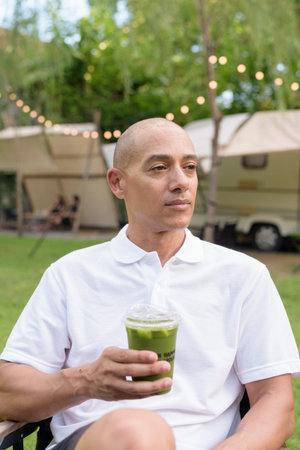 Stylish bald man in a white polo shirt relaxing at a campsite beside a camper van. Outdoor travel...