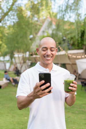 Stylish bald man in a white polo shirt relaxing at a campsite beside a camper van. Outdoor travel...