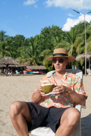 Man wearing a straw hat and Hawaiian shirt, dressed in casual summer vacation style. He poses at beach, showing a relaxed holiday atmosphere with resort fashion for beach or island travel.の写真素材