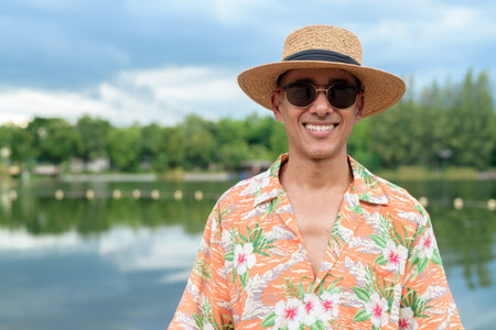 Man wearing a hat and Hawaiian shirt, dressed in casual summer vacation style. He poses at the beach, showing a relaxed holiday atmosphere with resort fashion for beach or island travel.の写真素材