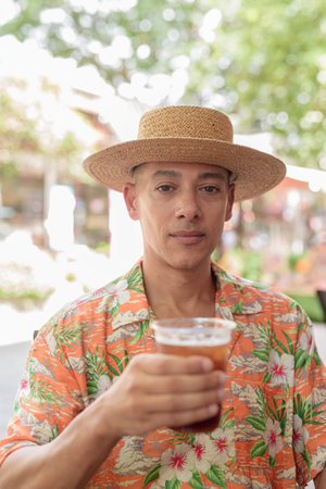 A Hispanic male tourist enjoying an iced coffee while sitting at an outdoor cafe on a sunny day,...
