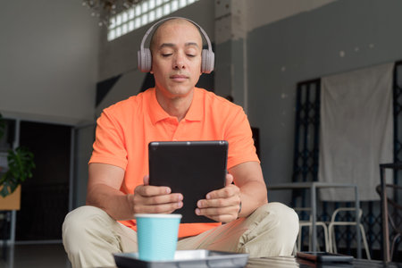 Happy man using tablet computer in coffee shop while wearing headphones listening music